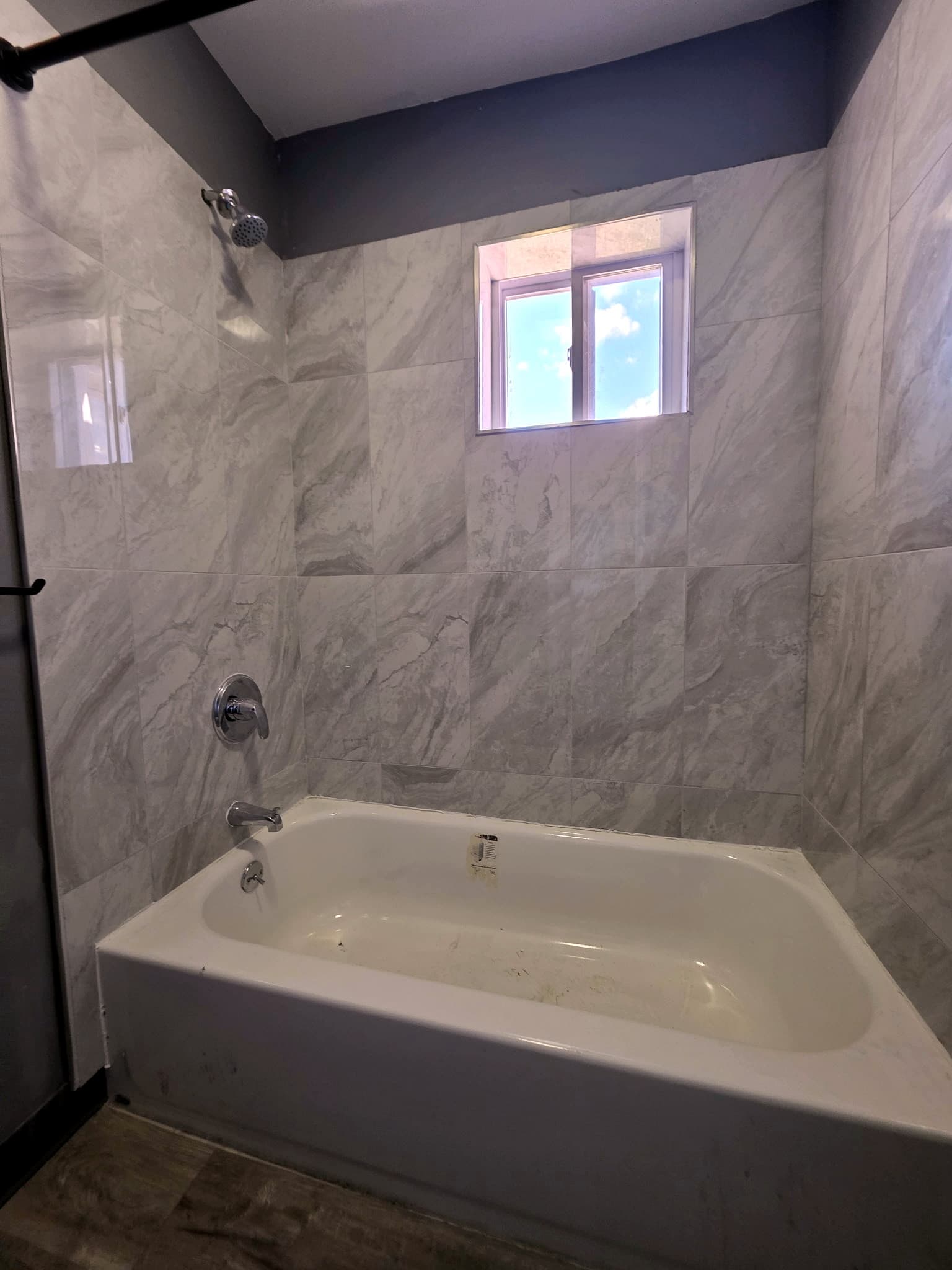 Bathroom with a white tub, marble-pattern tile, and a small window.