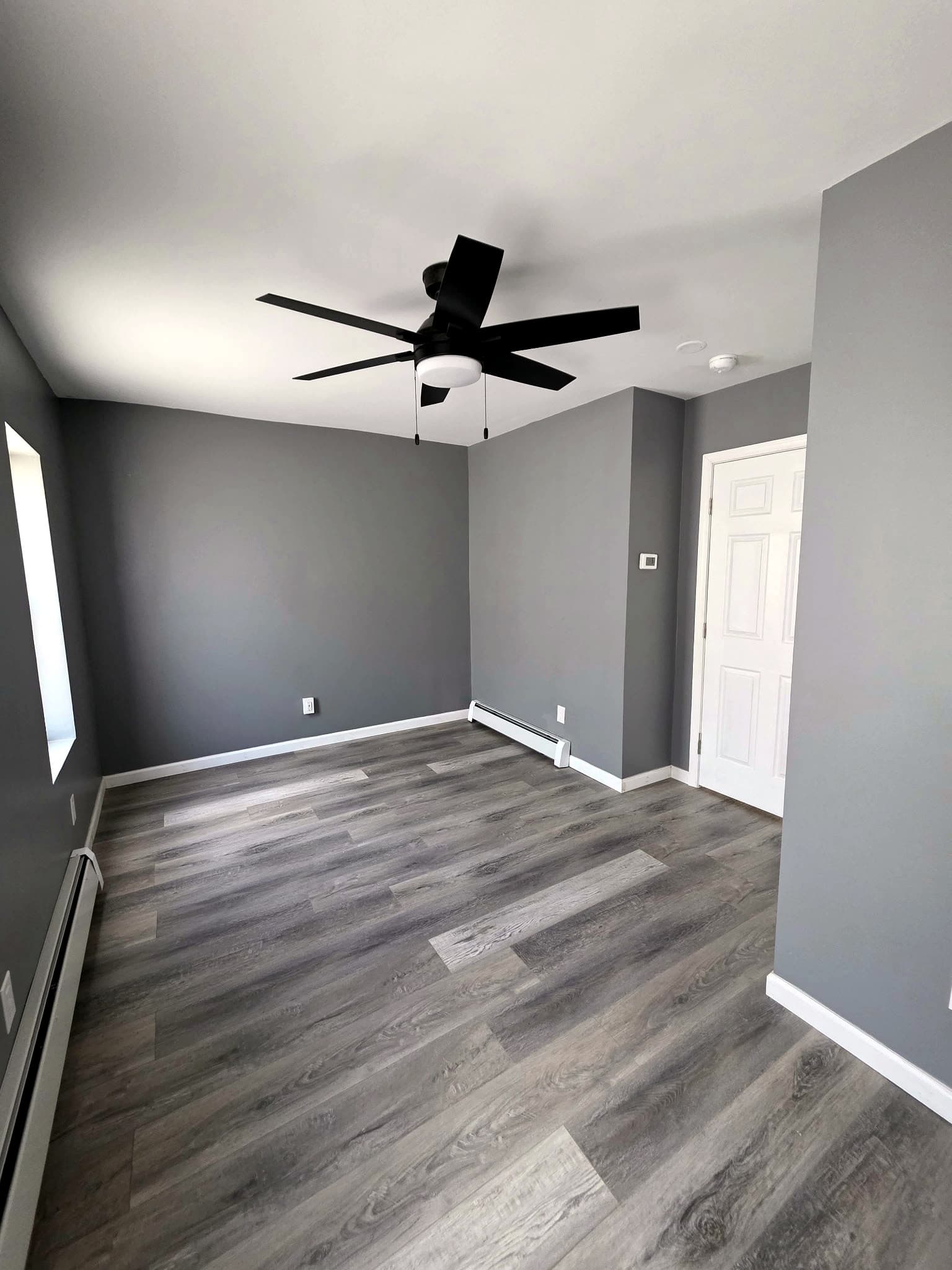 Empty room with a ceiling fan, a white door, and the edge of a window.